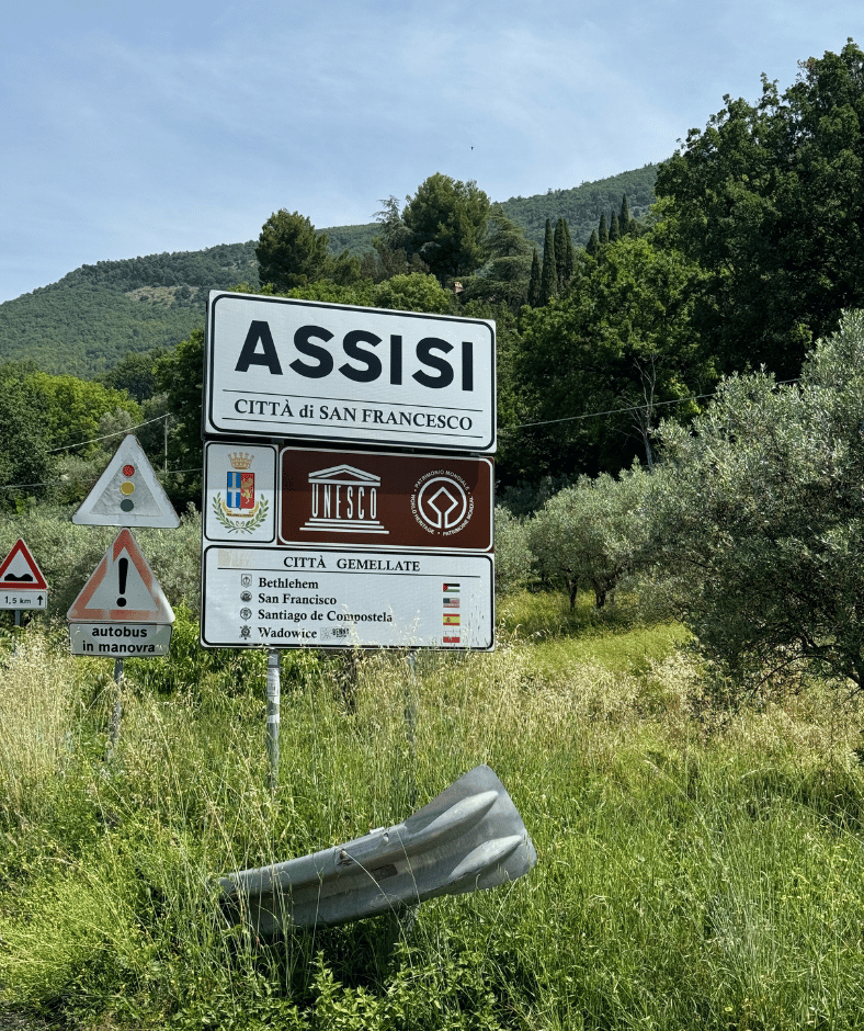 stadsbord met de naam assisi in het landschap langs de weg